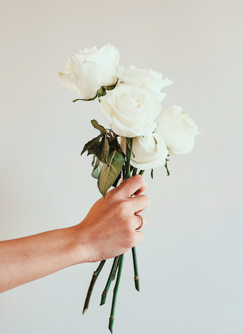 Image of a hand holding a bouquet of white roses against a white backdrop that leads to the Manifesting Love Category of the blog.